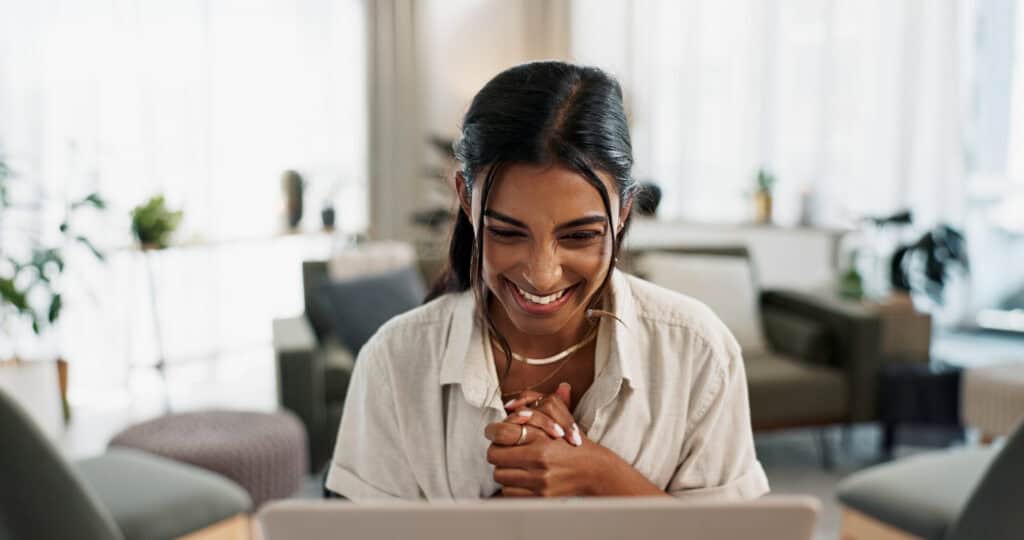 Laptop, woman and living room with excited for success in remote work, bonus and business feedback. Computer, technology and indian person as freelancer, happy and reading manager report on project.