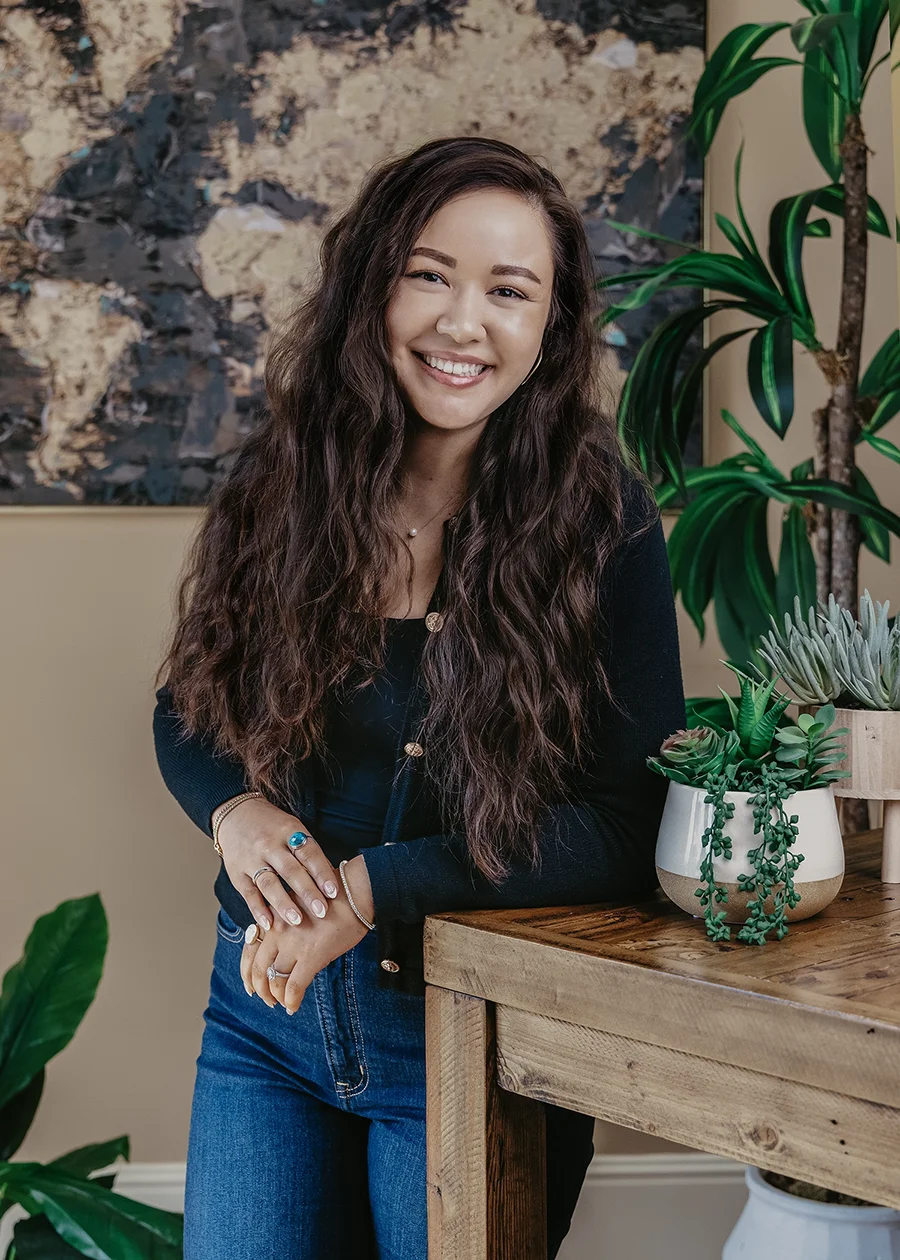 Photo of Hannah Welborn leaning against a bookshelf with a plant on it.